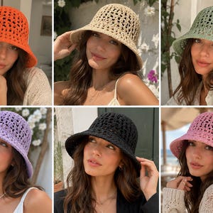 May include: A collection of six crochet bucket hats in various colours including orange, beige, light green, lavender, black, and pink. Each hat features an open-knit pattern with a rounded crown and a downward-sloping brim, crafted from yarn.