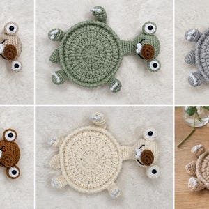 May include: A collection of six crocheted coasters shaped like turtles, each featuring a circular body, four small legs, and a head with two eyes and a brown nose. The coasters are available in beige, sage green, gray, dark brown, and cream colors.