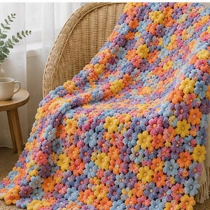 May include: A handmade crochet blanket featuring a dense pattern of three-dimensional flowers in shades of yellow, orange, light blue, and lavender. The textile is constructed from individual floral motifs joined together to create a textured surface.