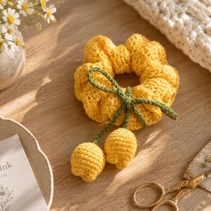 Può includere: Un elastico per capelli all'uncinetto giallo brillante con uno stelo all'uncinetto verde scuro e due piccoli boccioli di fiori gialli all'uncinetto attaccati sul davanti. L'accessorio ha un motivo a maglia a coste e forma circolare.