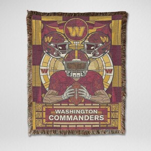 May include: A woven throw blanket with a football player holding a ball, two helmets, and the Washington Commanders logo. The design uses burgundy, gold, and brown colours, with a fringed edge. The words "Washington Commanders" are at the bottom.