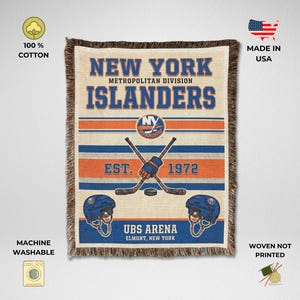 May include: A woven cotton throw blanket featuring the New York Islanders logo, text reading "NEW YORK ISLANDERS METROPOLITAN DIVISION", "EST. 1972", and "UBS ARENA ELMONT, NEW YORK". The design includes two crossed hockey sticks, a puck, and two helmets.