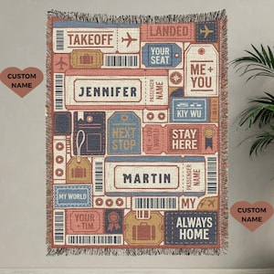 Könnte beinhalten: Eine gewebte Wurfadecke mit einem Reisemotiv. Die Decke zeigt verschiedene Ticket- und Etikettenillustrationen in Rot-, Blau- und Beigetönen. Der Text enthält "Takeoff", "Landed", "Jennifer", "Martin" und "Always Home".