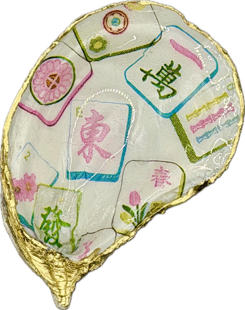 K&ouml;nnte beinhalten: Eine Austernschale, verziert mit einem wei&szlig;en Stoff mit bunten Mahjong-Kachel-Designs. Die Kacheln haben rosa, gr&uuml;ne und blaue Akzente. Der Rand der Schale ist mit Blattgold verziert.
