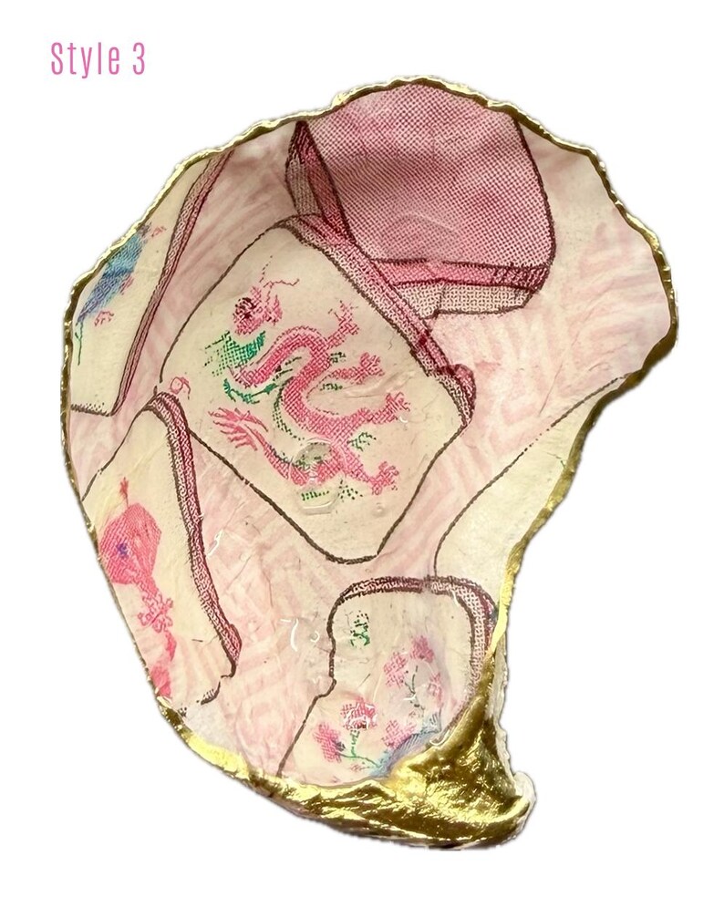 Puede incluir: Un plato decorativo de concha de ostra con un dise&ntilde;o de decoupage en patrones rosas y blancos, que incluye una ilustraci&oacute;n central de un drag&oacute;n rosa. Los bordes de la concha est&aacute;n pintados con un acabado dorado met&aacute;lico. El texto Style 3 es visible.
