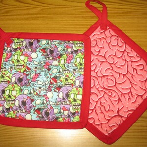 May include: Two red pot holders with a red border. One pot holder has a pattern of cartoon zombie faces. The other pot holder has a pattern of a pink brain.