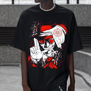 May include: Black t-shirt featuring a red and white graphic of a skull wearing a hat and sunglasses, with a cigarette and hand gestures. The design includes a compass rose and decorative elements.