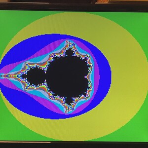 Puede incluir: Un monitor de computadora que muestra un fractal del conjunto de Mandelbrot a color. La forma negra central est&aacute; rodeada por capas conc&eacute;ntricas de azul, morado y amarillo sobre un fondo verde brillante. El texto OK es visible arriba a la izquierda.