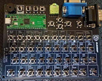Puede incluir: Un teclado de placa de circuito impreso negro con un microcontrolador Raspberry Pi Pico verde, un puerto VGA azul y un conector de audio verde. La placa está etiquetada como piSpectrum 2026 V 1.0 e incluye numerosos botones táctiles con etiquetas blancas.
