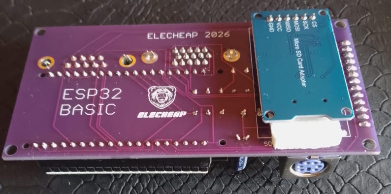 Puede incluir: Una placa de circuito impreso ESP32 BASIC de color morado con el texto ELECHEAP 2026 y un logotipo de oso, que incluye un m&oacute;dulo adaptador de tarjeta Micro SD azul a la derecha, con pines met&aacute;licos, un conector blanco y un puerto circular.