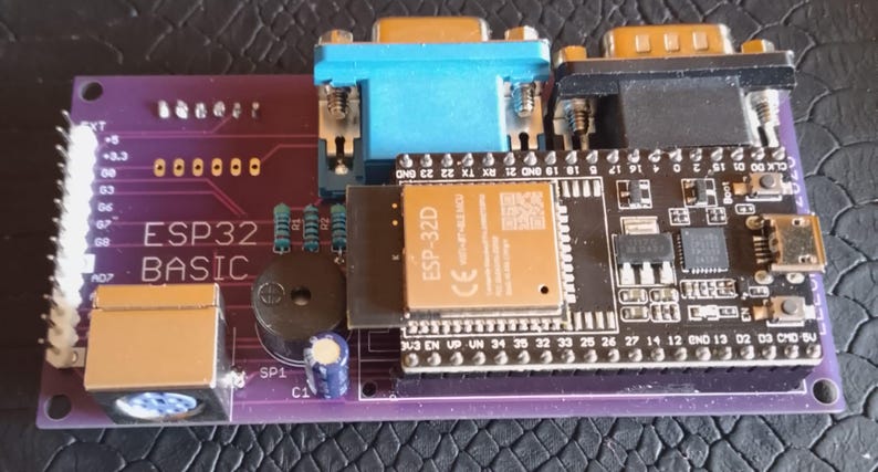 Puede incluir: Una placa de circuito impreso morada ESP32 BASIC que cuenta con un m&oacute;dulo de microcontrolador negro, un puerto VGA azul, un puerto serie negro, un zumbador circular, un conector de alimentaci&oacute;n y varios componentes electr&oacute;nicos con etiquetas blancas.
