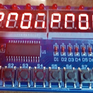 Può includere: Una scheda di circuito blu con display LED rossi che mostrano "P00.8.888". Presenta pulsanti, LED e il testo "LED & KEY". Probabilmente per elettronica o programmazione.