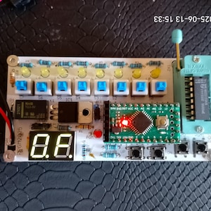 Peut inclure: Une carte de circuit imprimé avec divers composants électroniques, notamment des boutons bleus, des LED et un affichage numérique indiquant "8.8." Une petite carte de circuit imprimé verte avec une lumière rouge est également présente. Des fils et un support de puce sont visibles.