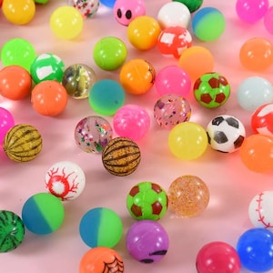 May include: A large collection of colorful bouncy balls with various designs, including a watermelon, a soccer ball, a smiley face, and a glittery ball.