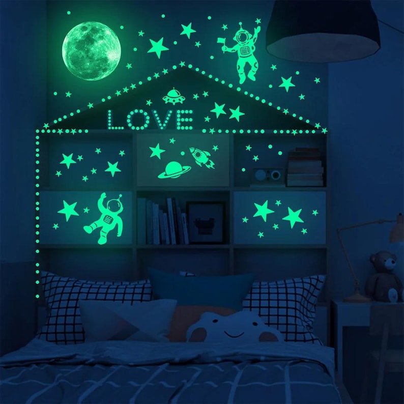K&ouml;nnte beinhalten: Leuchtende Wandaufkleber mit Sternen, Planeten, einer Rakete, einem UFO und Astronauten. Die Aufkleber sind in Form eines Hauses angeordnet, mit dem Wort "LOVE" in der Mitte.