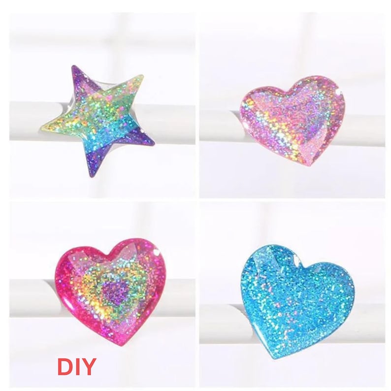 May include: Four resin rings with glitter embedded inside. The rings are shaped like a star and hearts. The star is rainbow colored. The hearts are pink, red, and blue.
