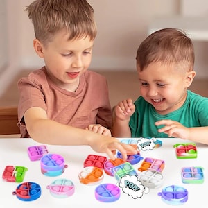 May include: Two children are playing with a selection of colourful pop-it fidget toys. The toys are made of silicone and come in various shapes and sizes. Some of the toys have the word "POP!" printed on them.