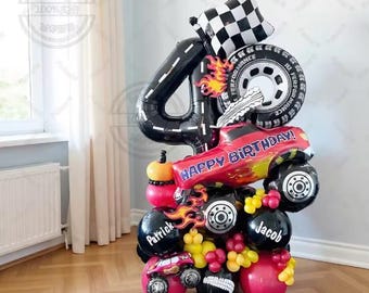 May include: A festive balloon arrangement for a fourth birthday celebration. The arrangement includes a black number 4 balloon, a checkered flag, a tire, and a red monster truck balloon that says "HAPPY BIRTHDAY!". Additional balloons are in red, black, and yellow.