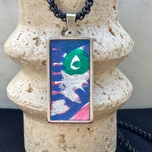 May include: A silver chain necklace with a rectangular pendant featuring abstract painted artwork in shades of blue, green, pink, and white.