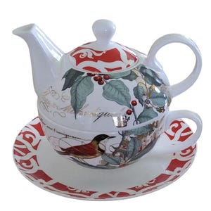 Pode incluir: Um conjunto de bule e xícara de chá de porcelana branca com um design floral vermelho e branco. O bule tem uma tampa e uma alça. A xícara tem uma alça e um pires. O conjunto apresenta um pássaro e bagas.