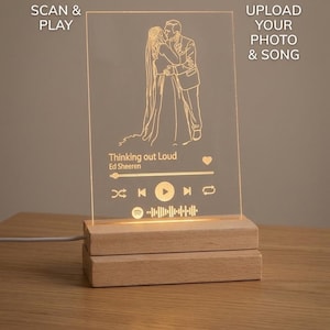 Könnte beinhalten: Personalisierte, beleuchtete Acrylplatte mit einer Silhouette eines Hochzeitspaares, dem Songtitel "Thinking out Loud" von Ed Sheeran und einem Spotify-Code. Die Platte steht auf einem Holzsockel. Text: "Scan & Play" und "Upload Your Photo & Song."