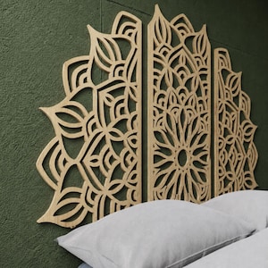 May include: Wooden wall art with a mandala design. The light-coloured wood artwork is made of three panels. The intricate design includes floral and geometric patterns, mounted on a dark green wall above two grey pillows.