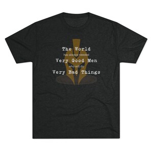 May include: Dark gray t-shirt with the text "The World has always needed Very Good Men who will do Very Bad Things" in white. A gold and brown graphic is centered below the text. The shirt has a crew neck and short sleeves.