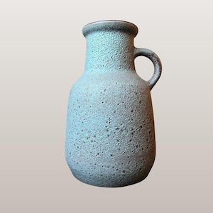 Op de afbeelding: Een lichtblauwe keramische vaas met een textuur en een handvat. De vaas is 20 cm hoog en heeft een afgeronde body met een smalle hals. De afbeelding bevat de tekst "WGP185 Unknown Studio Pottery | 110 | 20cm tall."