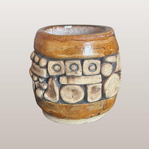 May include: A Studio Pottery vase, approximately 10cm tall, with a textured tan and brown design. The vase has a unique, layered pattern reminiscent of the Flintstones. The base is a lighter colour, and the rim is a darker brown.