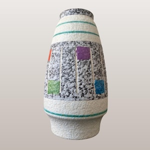 Peut inclure: Un vase en céramique avec un corps moucheté gris et blanc, orné d'accents carrés colorés. Le vase présente des bandes horizontales turquoise et blanches et une surface texturée. La base est blanche et le vase a une forme cylindrique.