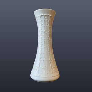 Può includere: Vaso in ceramica bianca con un design strutturato e gocciolante. Il vaso ha una base svasata e una parte superiore leggermente più ampia. Il testo "WGP065" e "KPM Bavaria "drizzle" vase | 678/2" sono visibili in basso.