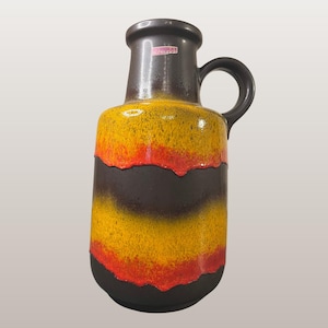 Puede incluir: Un jarrón de cerámica vintage con asa, con una combinación de colores amarillo, naranja y marrón. El jarrón tiene una parte superior e inferior marrón oscuro, con un diseño texturizado. El texto "WGP132 Scheurich 108/40" es visible.