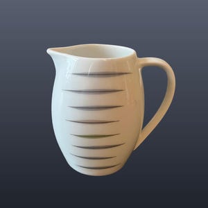 Może przedstawiać: Biały ceramiczny dzbanek do mleka z zakrzywionym uchwytem i dzióbkiem. Dzbanek jest ozdobiony poziomymi szarymi i zielonymi paskami. Ma 9 cm wysokości.