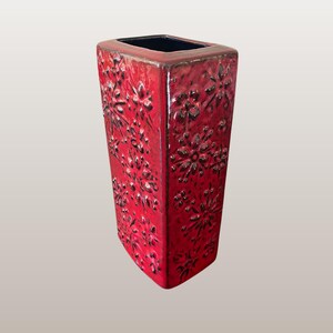 Peut inclure: Un vase en céramique rouge de forme carrée avec un intérieur noir. Le vase présente un motif floral et le texte "WGP170 Scheurich "Kosmos" 263/31".