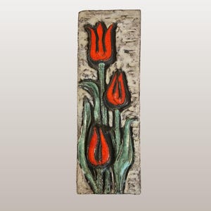 Può includere: Targa da parete rettangolare con tre tulipani rossi con steli e foglie verdi. Lo sfondo è strutturato e bianco sporco. La targa è intitolata "Ruscha | Tulip Wall Plaque".