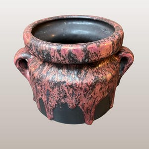 Könnte beinhalten: Ein schwarzer Keramiktopf mit einer rosa-schwarzen Glasur. Der Topf hat zwei Henkel und ist 10 cm hoch. Der Topf ist mit "WGP200 Otto Keramik | "Ätna" Dekor | 10cm hoch" beschriftet.