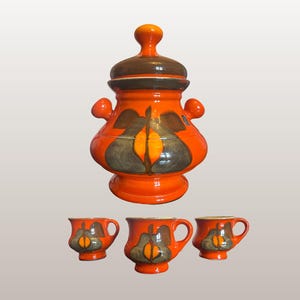 Könnte beinhalten: Ein orangefarbenes Keramik-Bowlegefäß mit Deckel und drei passenden Tassen. Die Bowle und die Tassen haben ein dekoratives Design in Braun-, Grau- und Orangetönen. Das Set ist ein Vintage-Design von Cortendorf 8613.