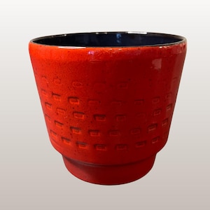 Puede incluir: Una maceta de cerámica roja vibrante con una superficie texturizada y un interior azul oscuro. La maceta presenta una serie de patrones cuadrados empotrados alrededor de su exterior. Mide aproximadamente 11,5 cm de alto, adecuada para plantas pequeñas o uso decorativo.