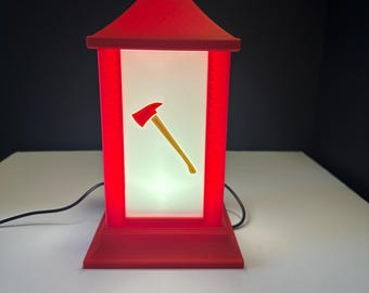 Pode incluir: Lâmpada vermelha em estilo pagode com um painel branco iluminado. Um gráfico de machado amarelo e vermelho está centrado no painel. A lâmpada tem uma base quadrada e um topo pontiagudo. Um cabo de alimentação preto sai da base.