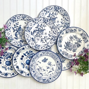 May include: A collection of eight white ceramic plates with blue floral and bird designs. Each plate features a different pattern, including birds, flowers, and fruit. The plates have a blue border and are arranged on a white surface.