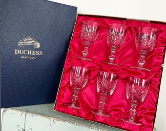 May include: A set of six clear glass wine glasses with a cut crystal design, packaged in a blue box with a gold crown and the text "Duchess Hand Cut".