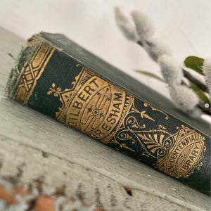 May include: Close-up of the spine of a green hardcover book with gold lettering that reads "GILBERT GRESHAM" and "SEMI-CENTENNIAL LIBRARY".