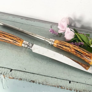 May include: A white ceramic mug with a black handle and the text "But First, Coffee" in a bold, black font. The mug is set against a blurred background, suggesting a cozy setting.