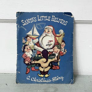 May include: Vintage children's book titled "Santa's Little Helpers" with a blue cover. The cover features an illustration of Santa Claus and several elves. The book is a Christmas story.