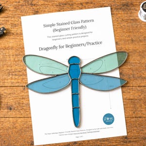 Pode incluir: Um padrão de libélula em vitral para iniciantes, com asas e corpo azuis e verde-azuis. O padrão está em uma folha de papel branca com o texto "Dragonfly for Beginners/Practice". Ferramentas de artesanato são visíveis.