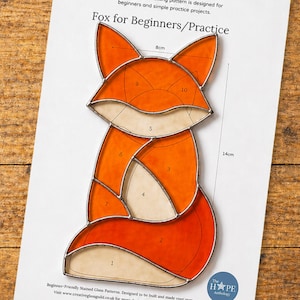 Puede incluir: Un patrón de zorro de vidriera para principiantes. El zorro es naranja y crema con un contorno plateado. El patrón mide 14 cm de alto y 8 cm de ancho. El texto "Fox for Beginners/Practice" está en la parte superior de la página.