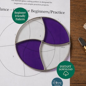 May include: A stained glass cutting pattern for beginners. The design features a circular shape with purple and white sections, held within a metal frame. The pattern is on a paper with the text "Balance" and "Beginner Friendly Pattern". The diameter is 14cm.
