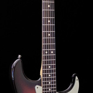 Pu&ograve; includere: Una chitarra elettrica Fender Stratocaster con finitura sunburst. La chitarra ha un manico in acero, battipenna bianco e tre pickup single-coil. Il logo Fender &egrave; sulla paletta.