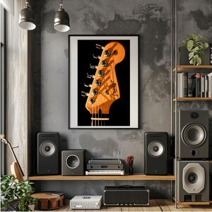 Pu&ograve; includere: Una stampa incorniciata di una paletta di chitarra con il logo Fender. La paletta &egrave; marrone chiaro con meccaniche argentate. La stampa &egrave; appesa a una parete grigia sopra una mensola con altoparlanti e apparecchiature audio.