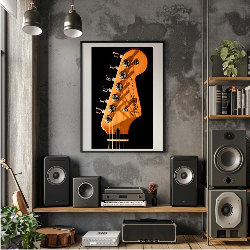 Pu&ograve; includere: Una stampa incorniciata di una paletta di chitarra con il logo Fender. La paletta &egrave; marrone chiaro con meccaniche argentate. La stampa &egrave; appesa a una parete grigia sopra una mensola con altoparlanti e apparecchiature audio.